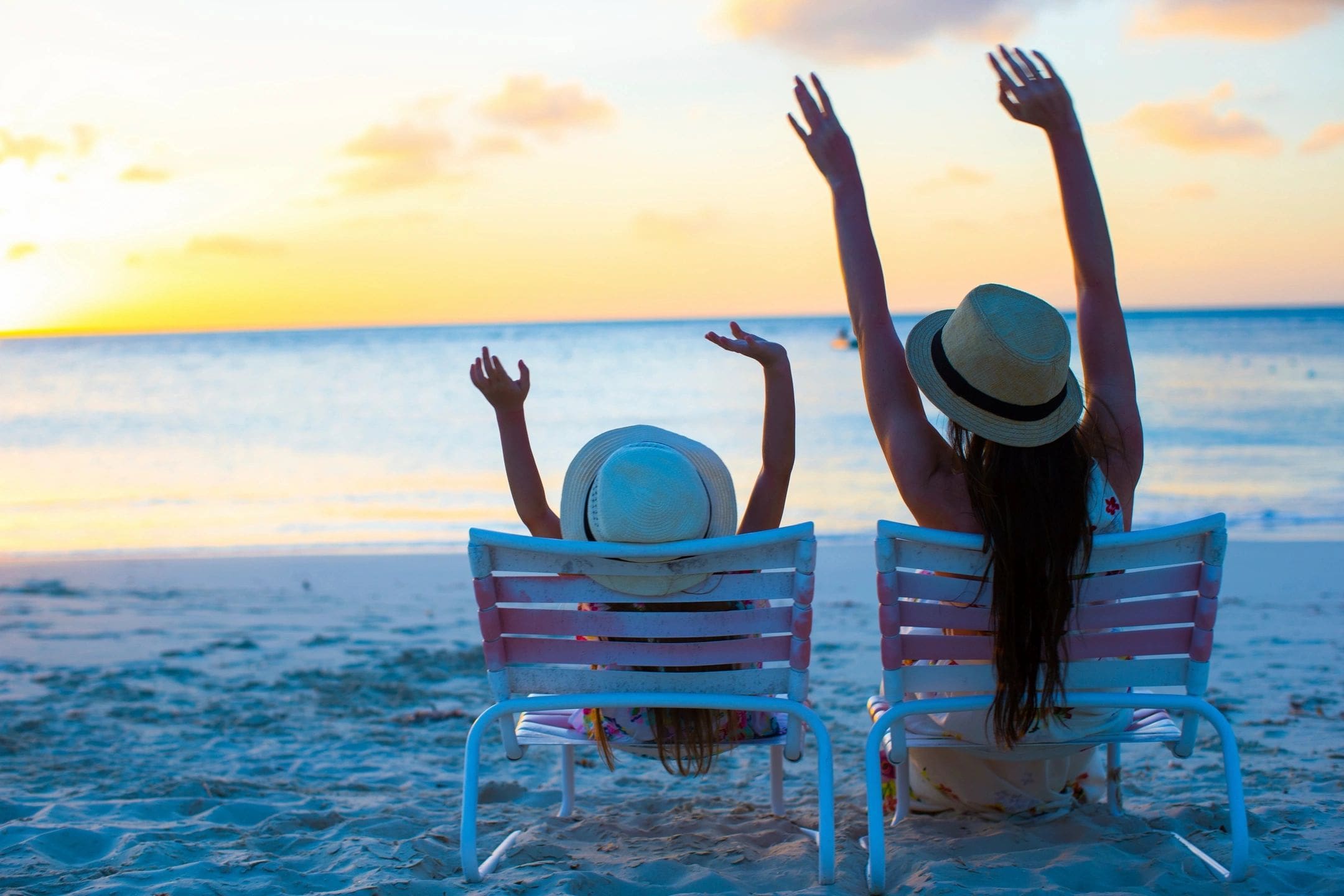 Two women sitting on beach chairs with arms up.